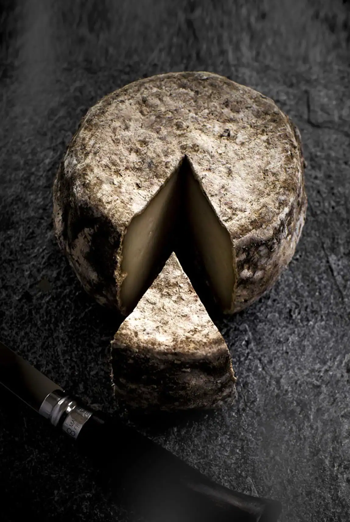 Fromage affiné découpé avec une portion et un couteau sur une surface sombre.