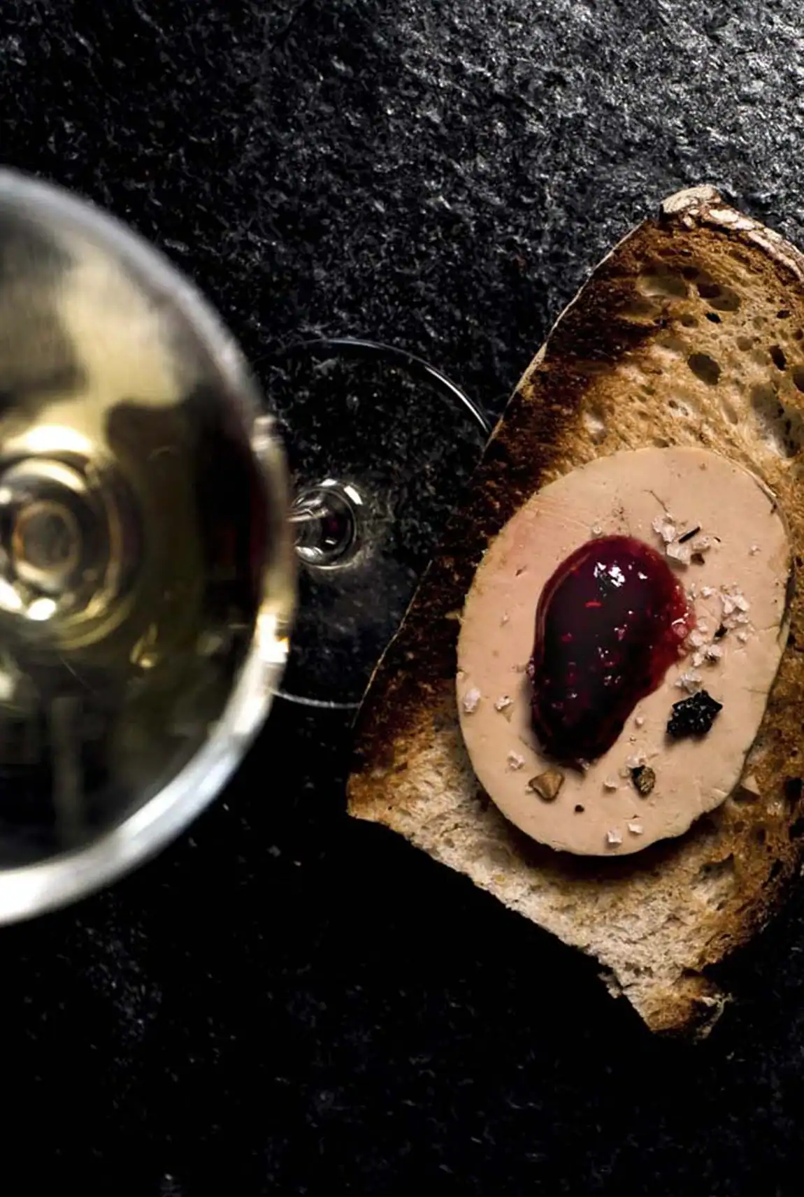 Verre de vin et mets artisanaux et couteau pr&eacute;sent&eacute;s sur une pierre sombre pour Le Cercle des Ar&ocirc;mes.