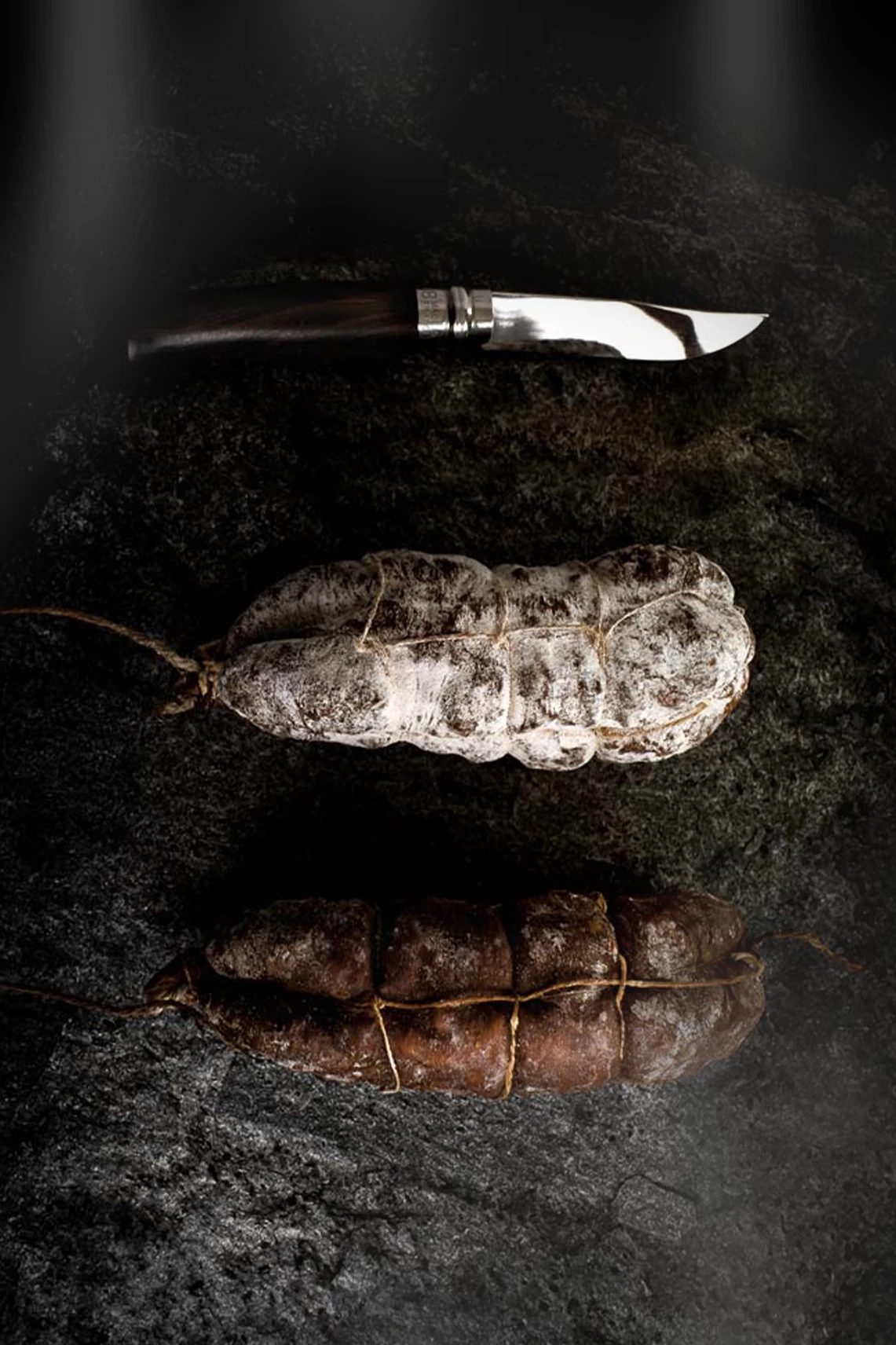 Saucissons artisanaux et couteau pr&eacute;sent&eacute;s sur une pierre sombre pour Le Cercle des Ar&ocirc;mes.
