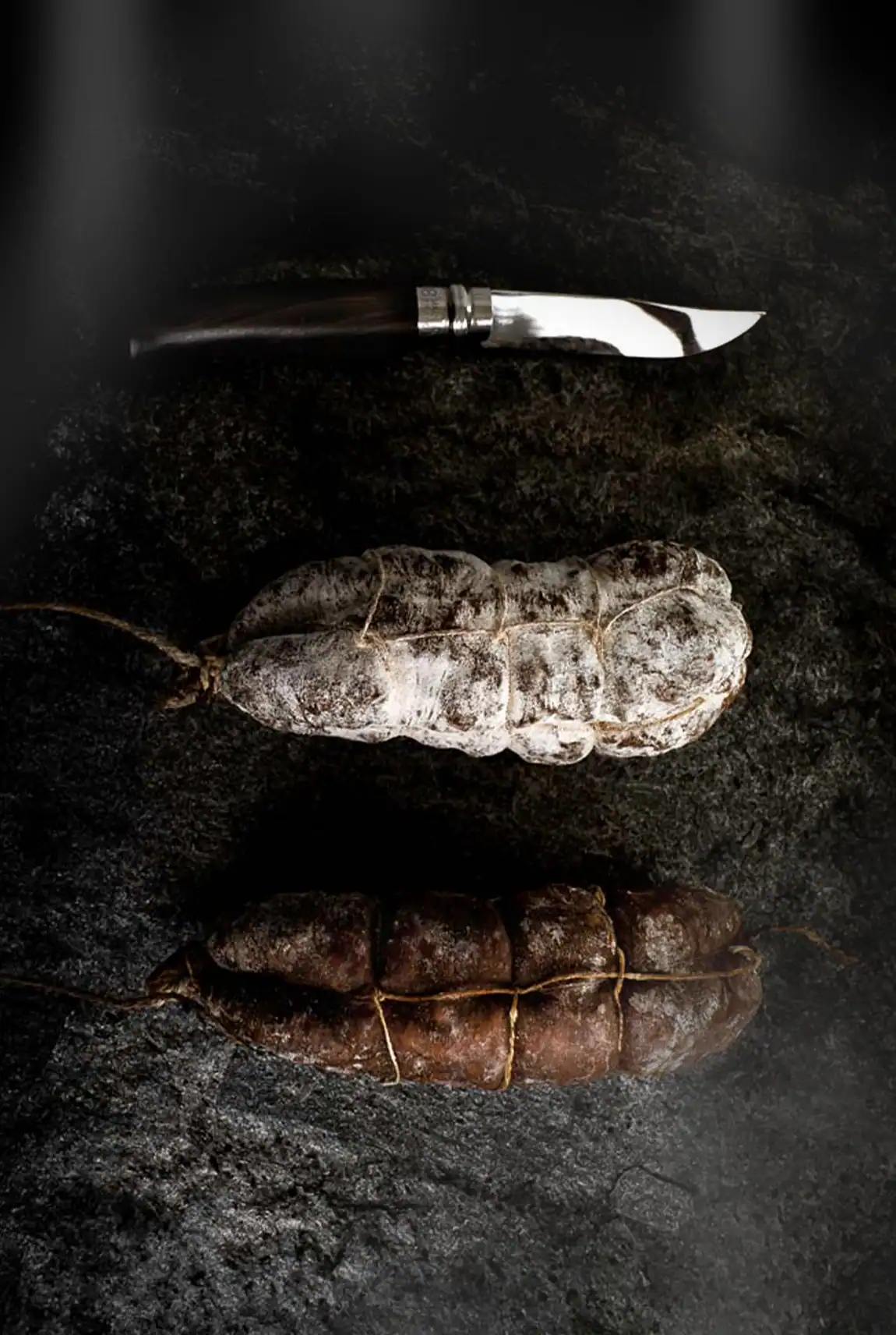 Saucissons artisanaux et couteau présentés sur une pierre sombre pour Le Cercle des Arômes.