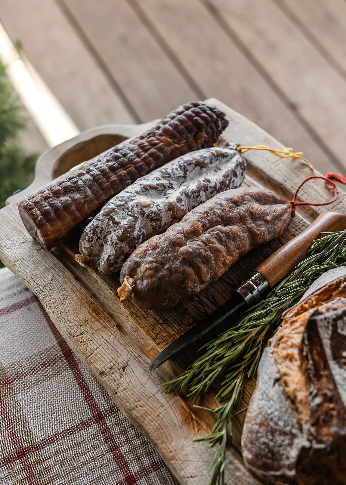 Trois saucissons secs artisanaux Maison Alpin présentés sur une planche en bois avec romarin et couteau.