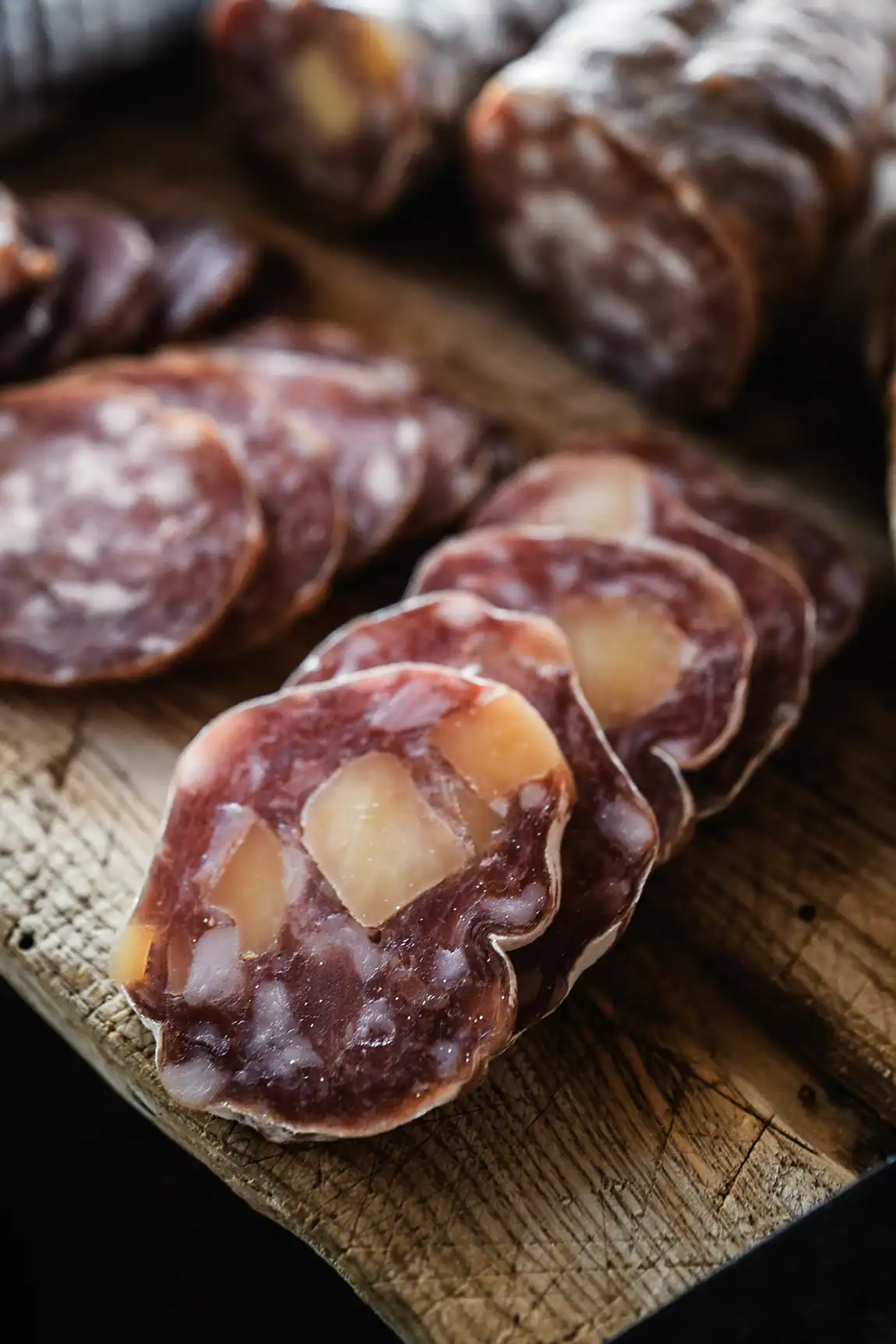 Saucisson artisanal Maison Alpin aux morceaux de fromage, tranch&eacute; sur une planche en bois.