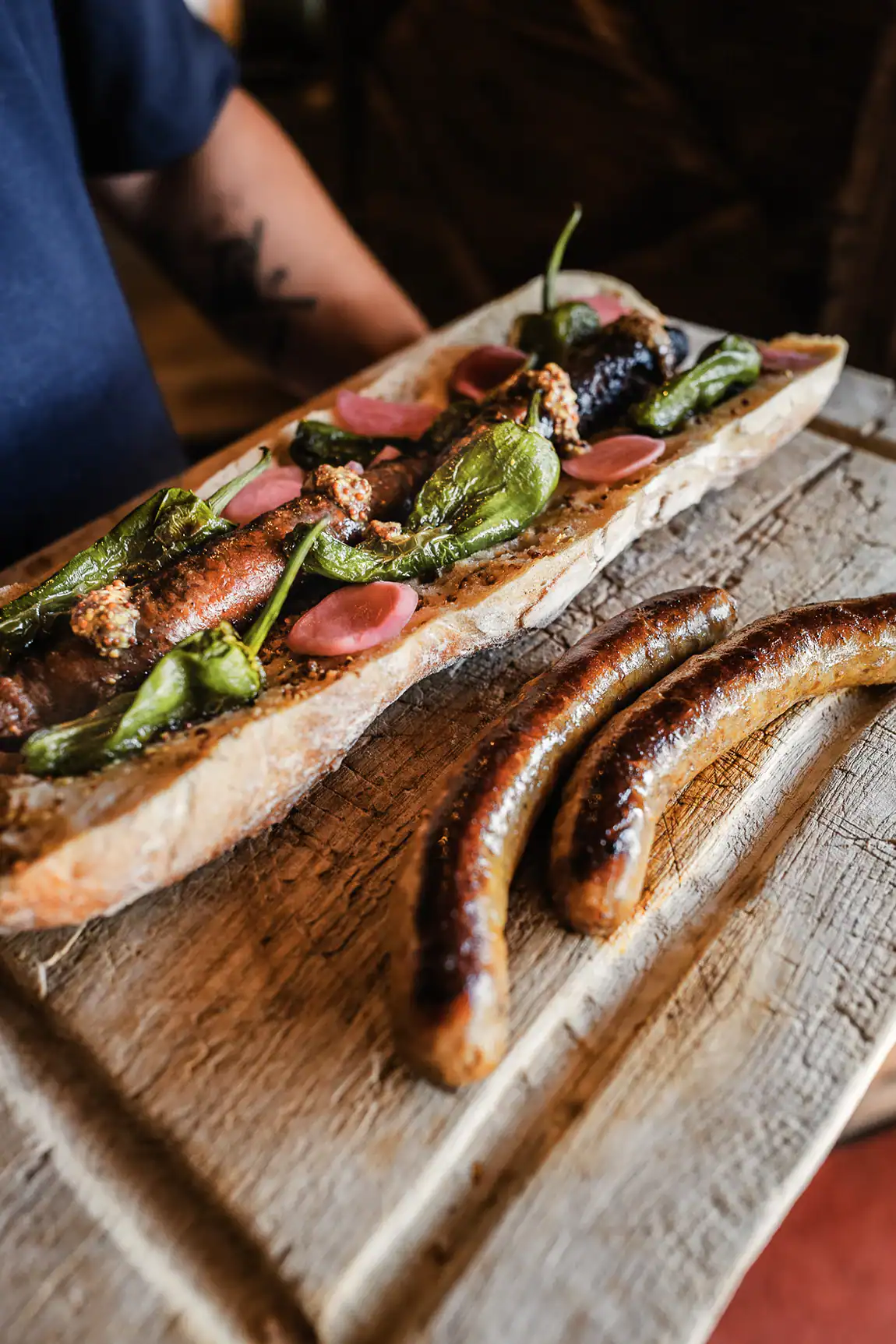 Diots grillés Maison Alpin servis avec poivrons, moutarde à l’ancienne et pickles sur une planche en bois.