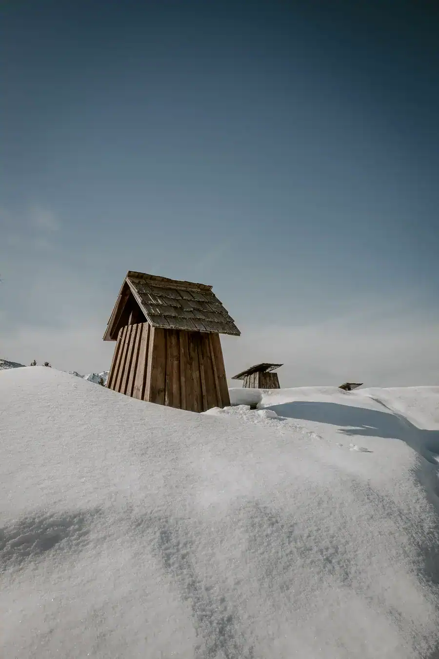 Bornes de cheminées savoyardes en bois sous la neige dans un alpage