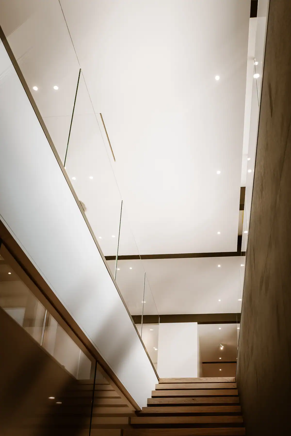 Escalier en bois, garde-corps en verre et volumes blancs dans une villa à Genève