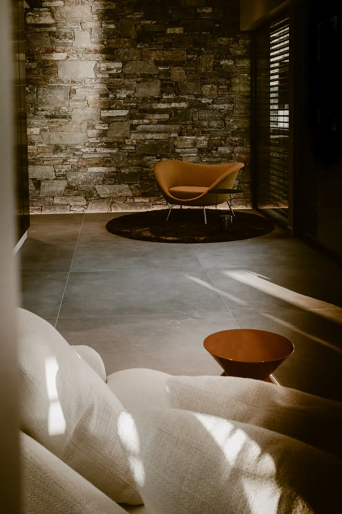 Salon contemporain avec fauteuil sculptural devant un mur en pierre naturelle