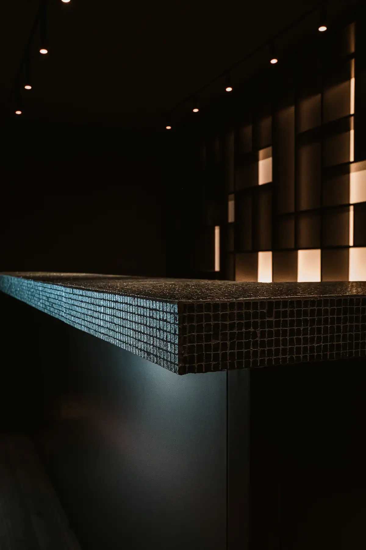 Comptoir contemporain habillé de petits carreaux sombres avec éclairage architectural