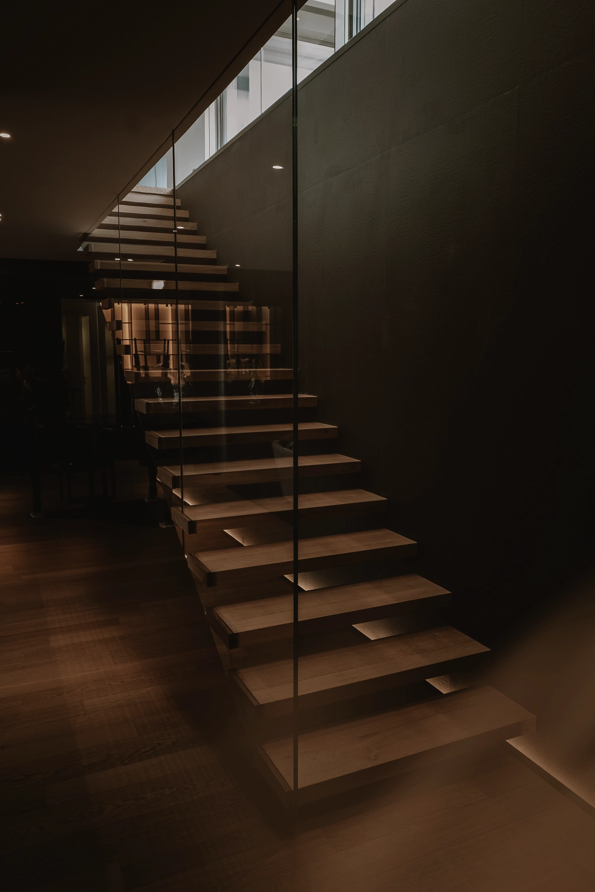 Escalier contemporain en bois suspendu derrière une paroi de verre