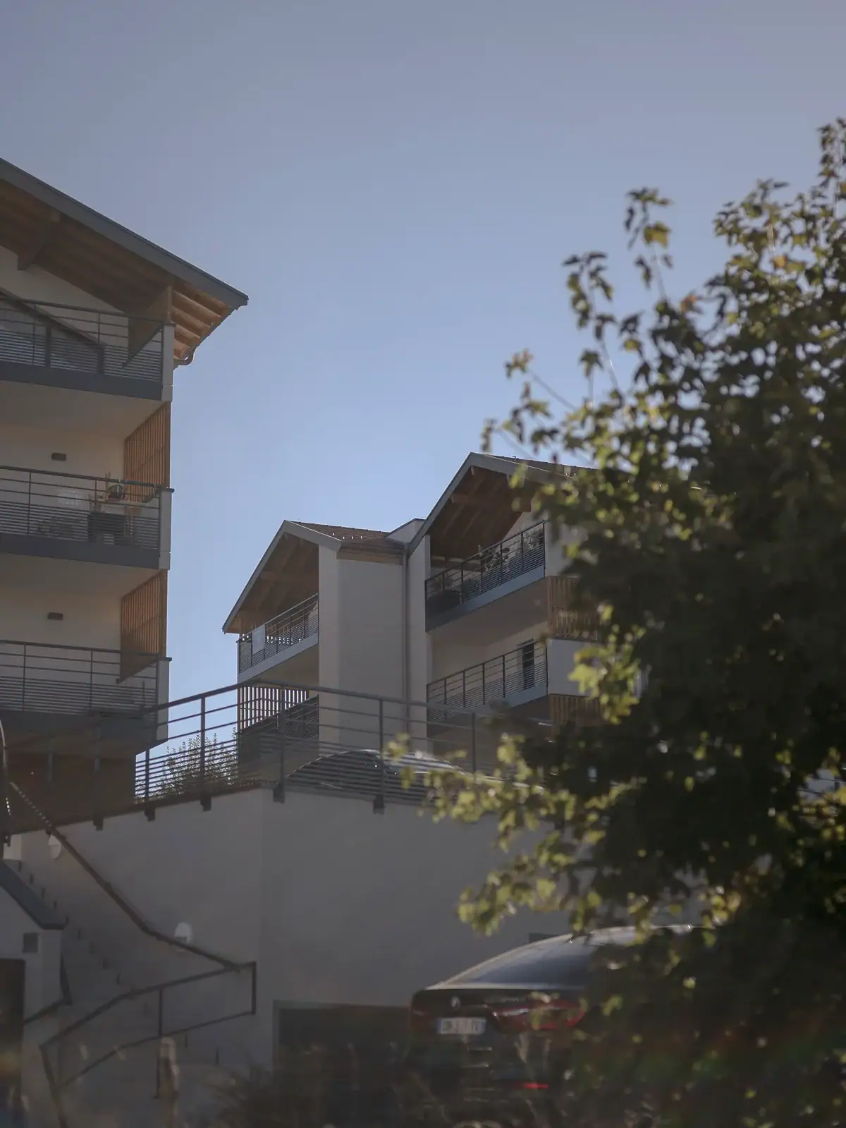 Bâtiments résidentiels Pré-Cosy à Villy-le-Pelloux, avec balcons, passerelles métalliques et bardages en bois, vus à travers la végétation.