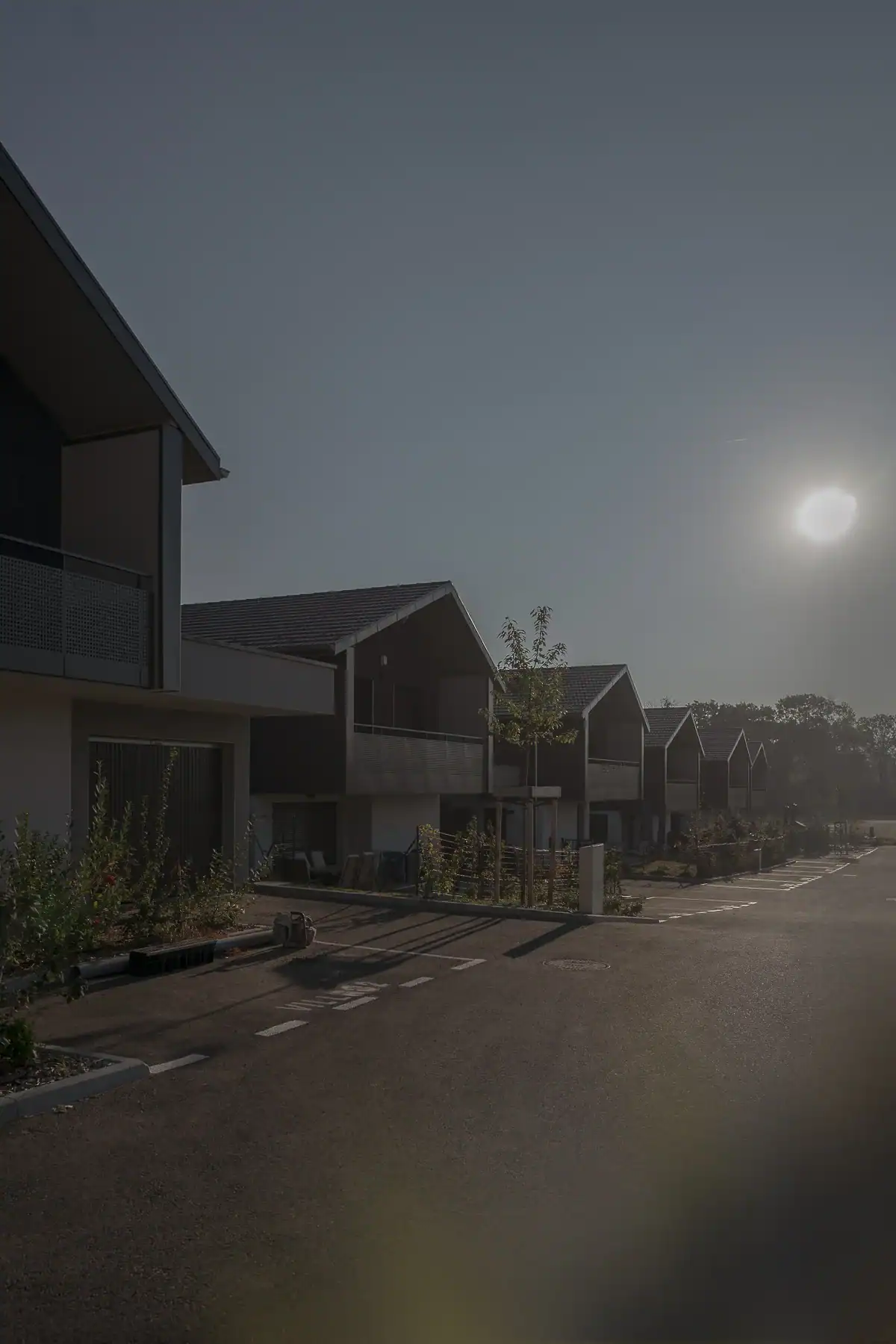 Alignement de maisons contemporaines à Versonnex, dans le Pays de Gex, avec toitures à deux pans et façades éclairées par le soleil bas.