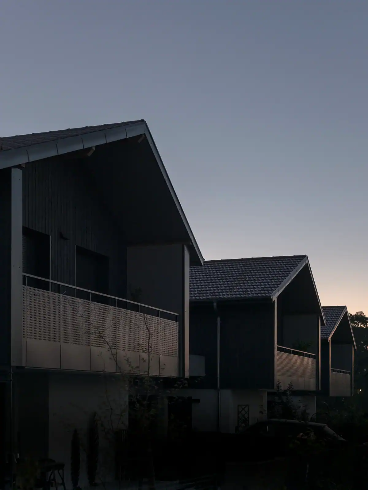 Façades de bâtiments résidentiels à Versonnex au crépuscule, avec bardages sombres, balcons métalliques et succession de toitures.